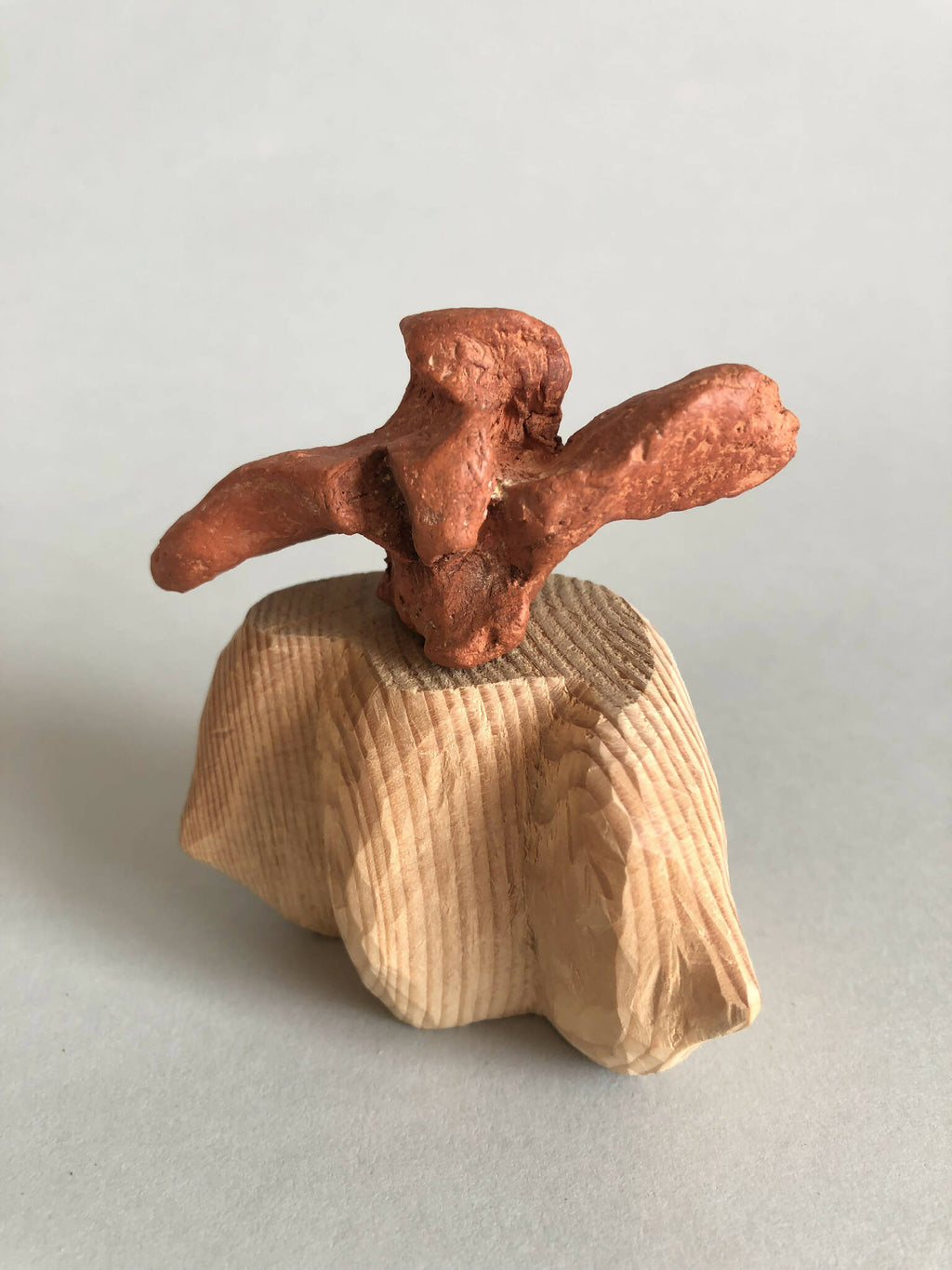 Petit socle sculpté beige avec petite figurine brune en relief, surmontée d’un motif