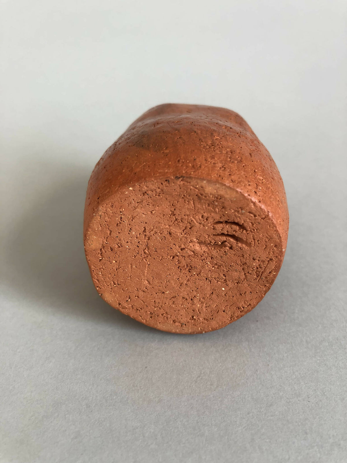 Petit vase en terre cuite orange, base arrondie, surface frottée.