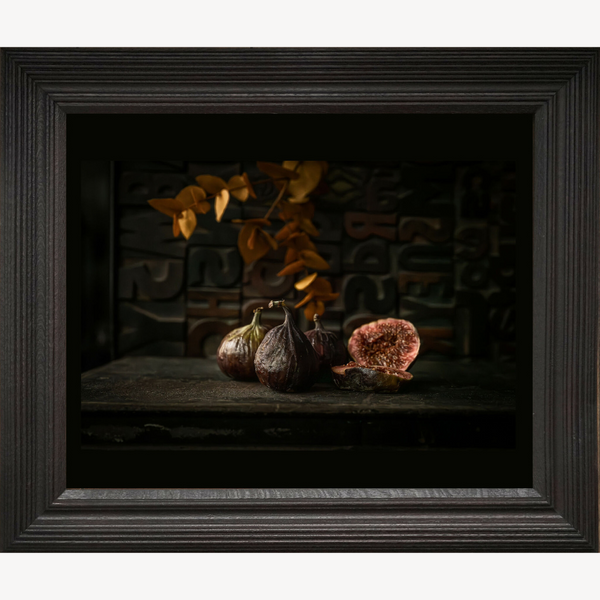 Tableau nature morte encadré montrant figues entières et figue tranchée sur socle sombre