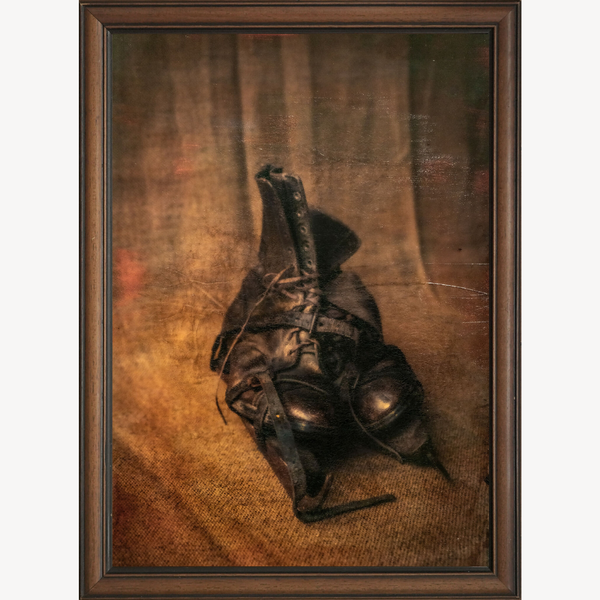 Tableau encadré de bottes sombres et patin métallique, composition sur fond brun.