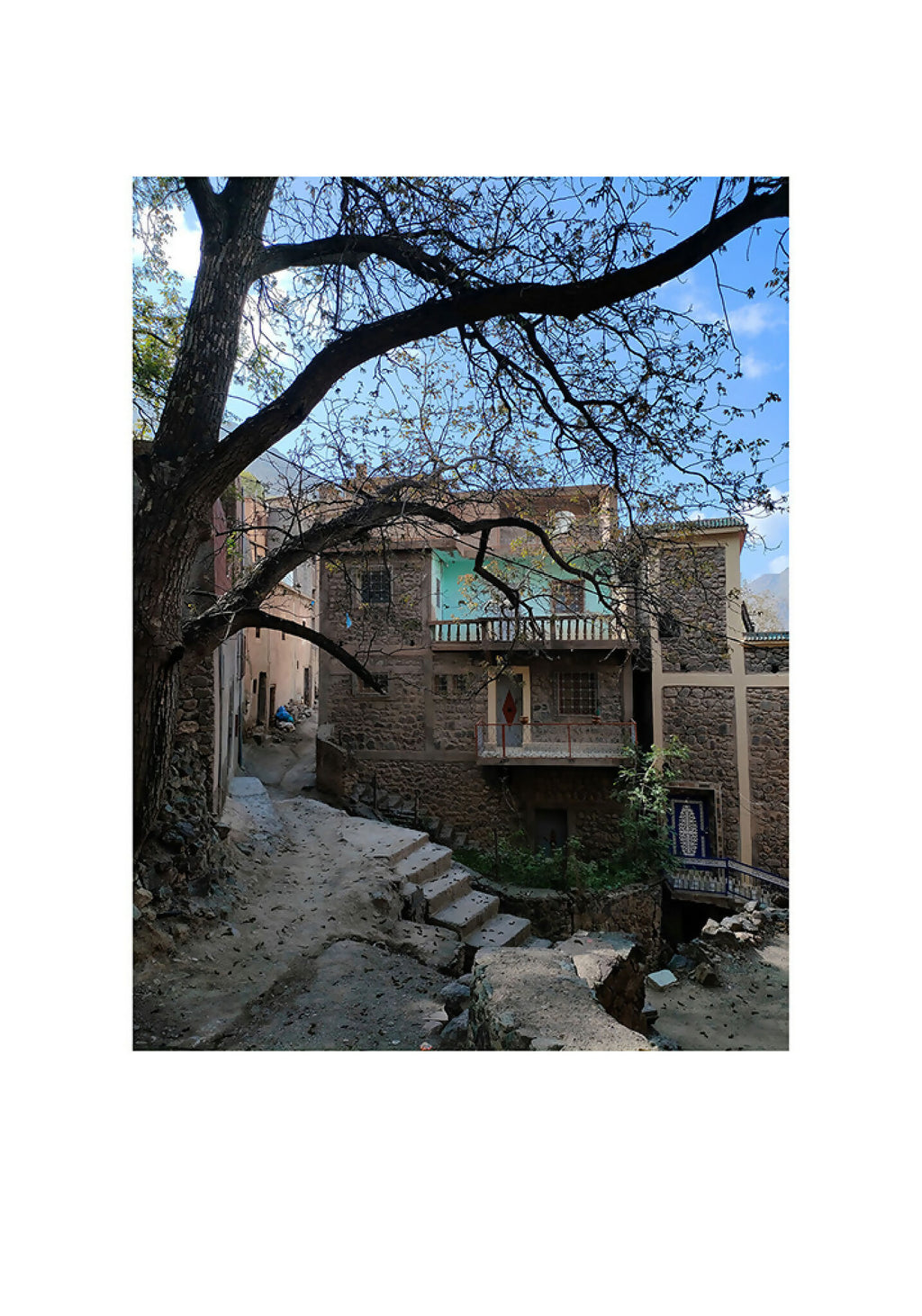 Tirage photo vertical : ruelle en pierre sous un ciel bleu, arbre aux branches.