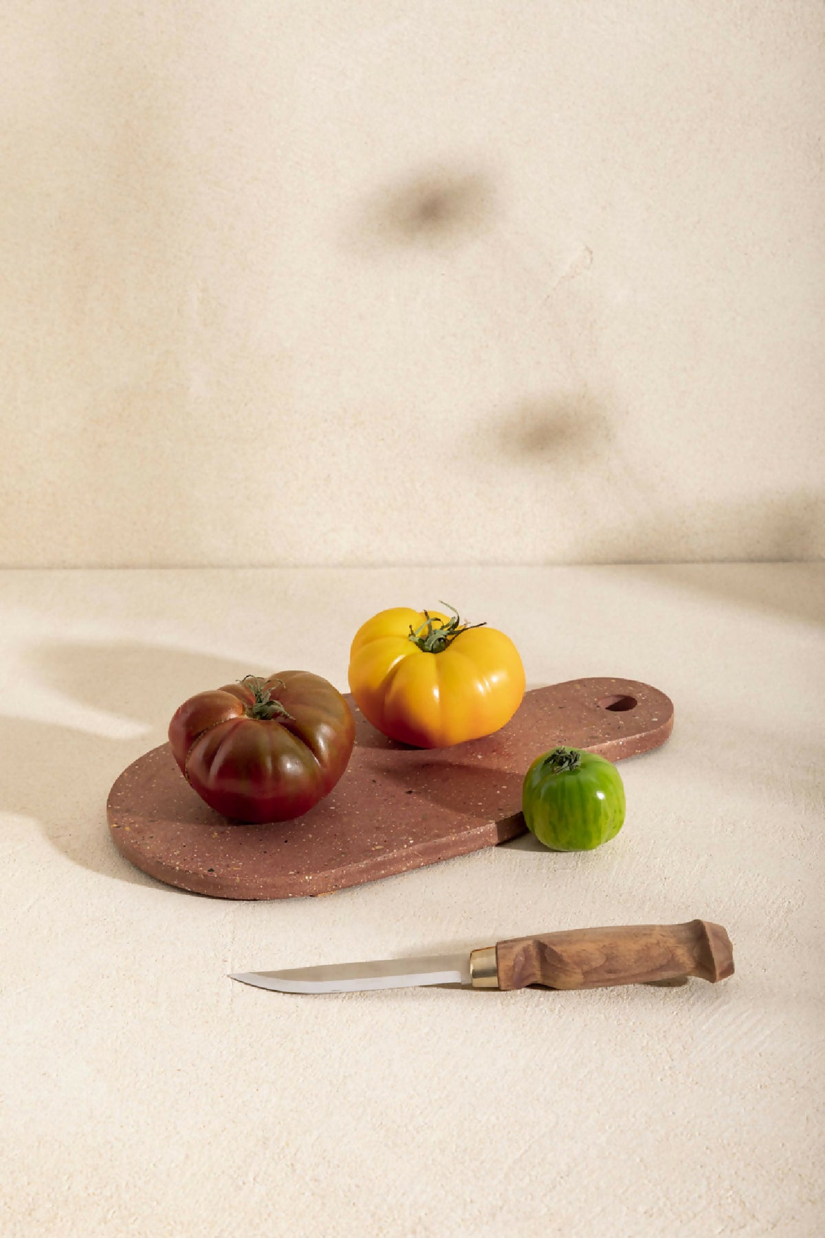 Planche à découper AIMÉE brun foncé avec trou, couteau et tomates décoratives.