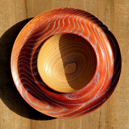 Coupe à fruits en bois, plateau circulaire orange à rayures, anneau central clair.