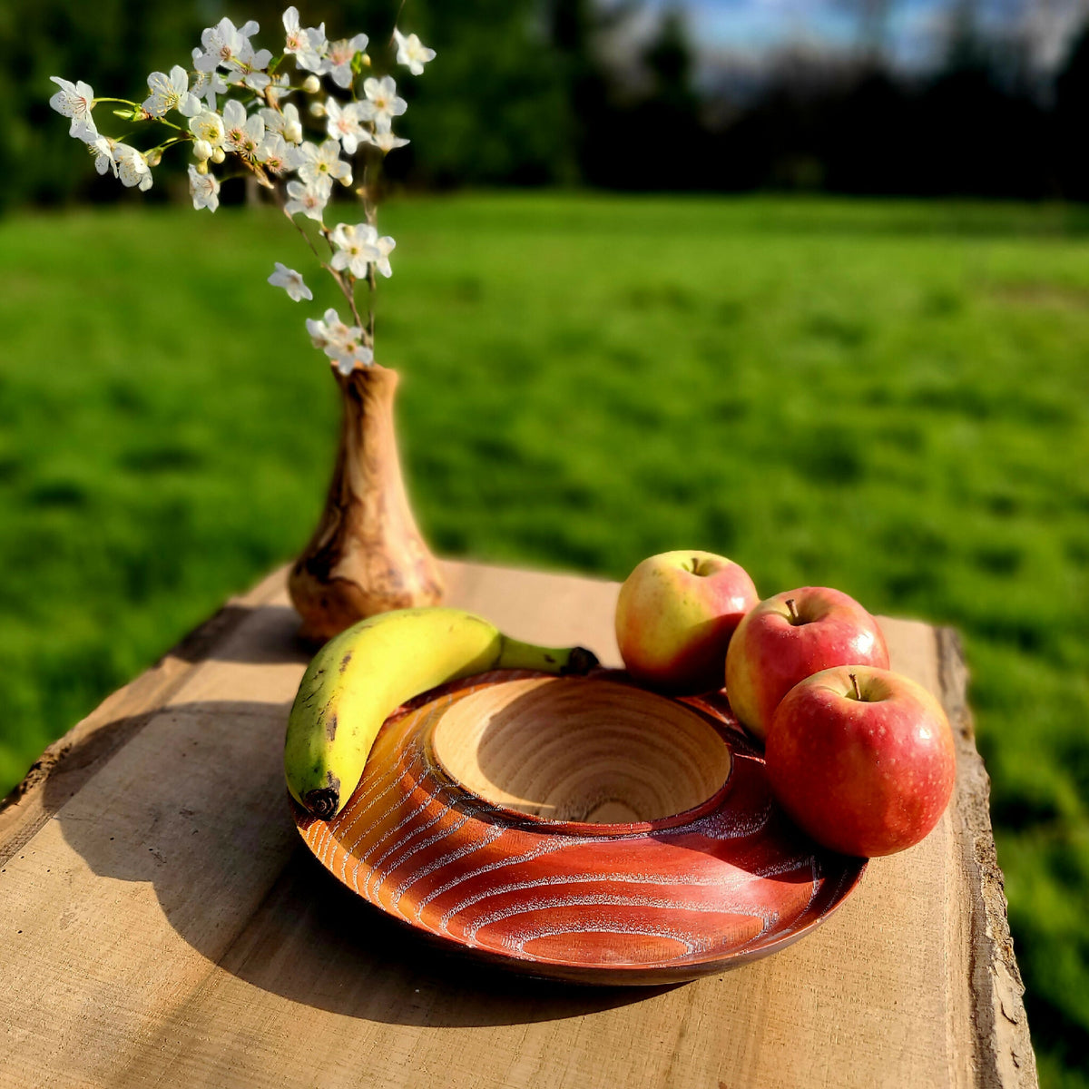 Coupe à fruits en bois strié orange, remplie de pommes et banane.