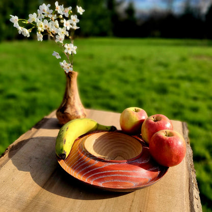 Coupe à fruits en bois strié orange, remplie de pommes et banane.