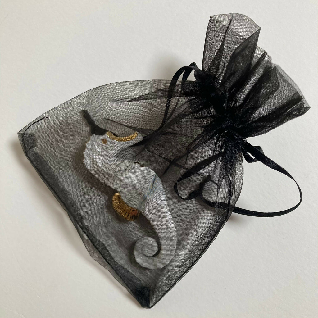 Porte-couverts hippocampe blancs et dorés dans un sachet en organza noir.