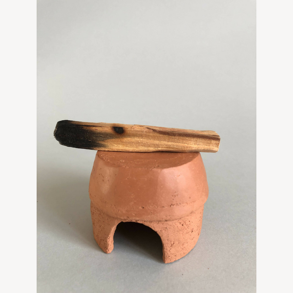 Petit pot en argile terracotta avec ouverture frontale, branche en bois sur le dessus.