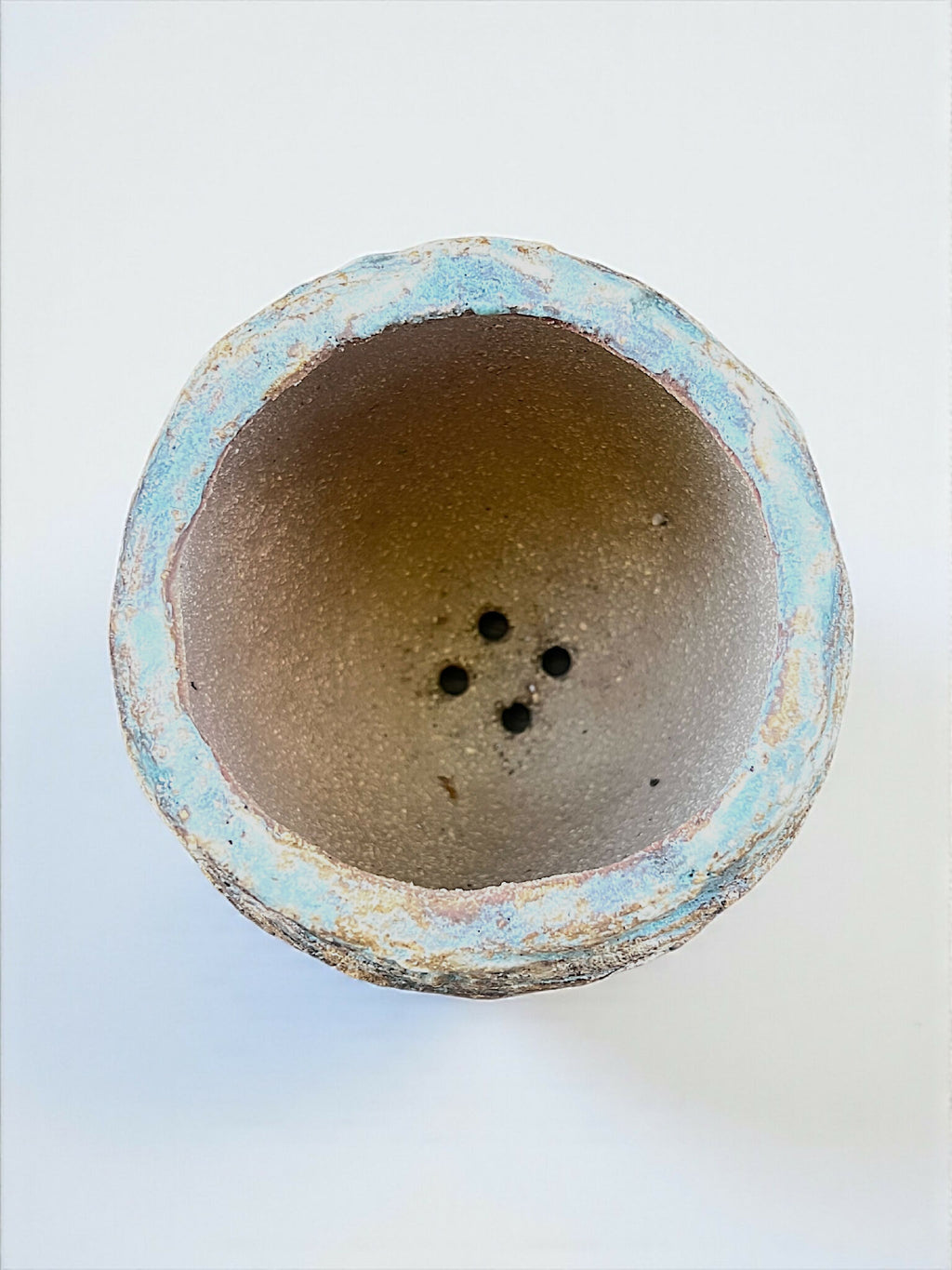 Base de pot en grès bleu turquoise, intérieur brun, trois trous de drainage visibles.