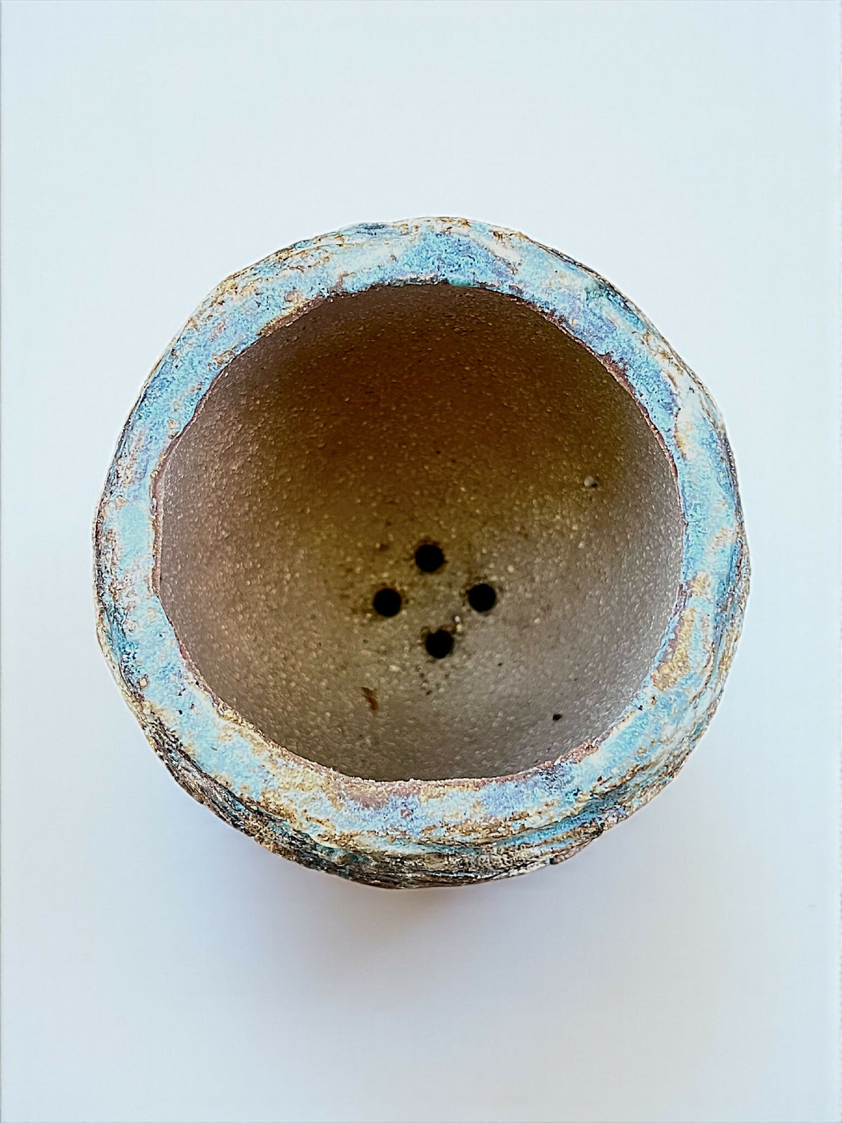 Base de pot en grès turquoise, intérieur brun granuleux, trois trous de drainage.