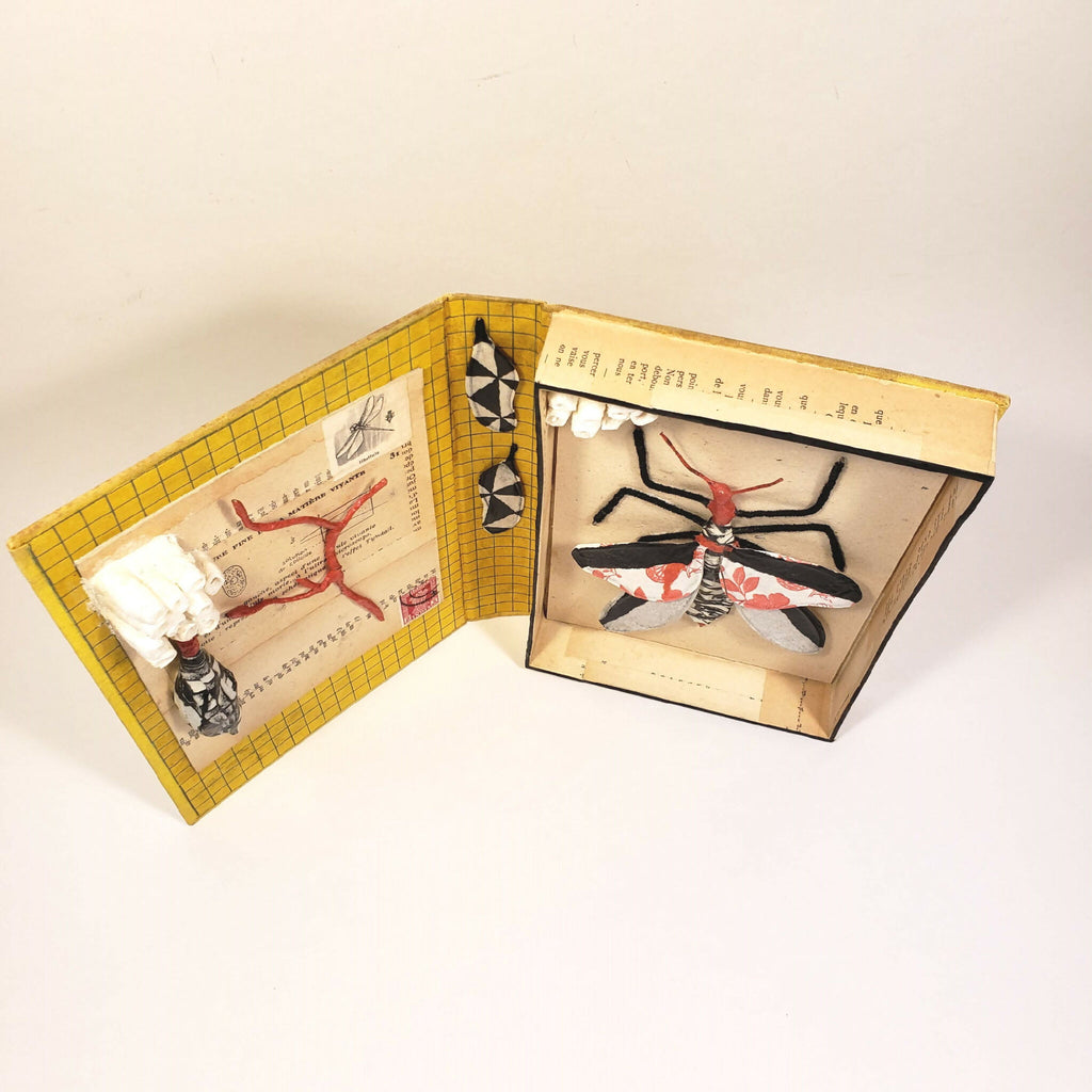 Livre jaune sculpté, vue de profil avec pages ouvertes et insecte en relief.
