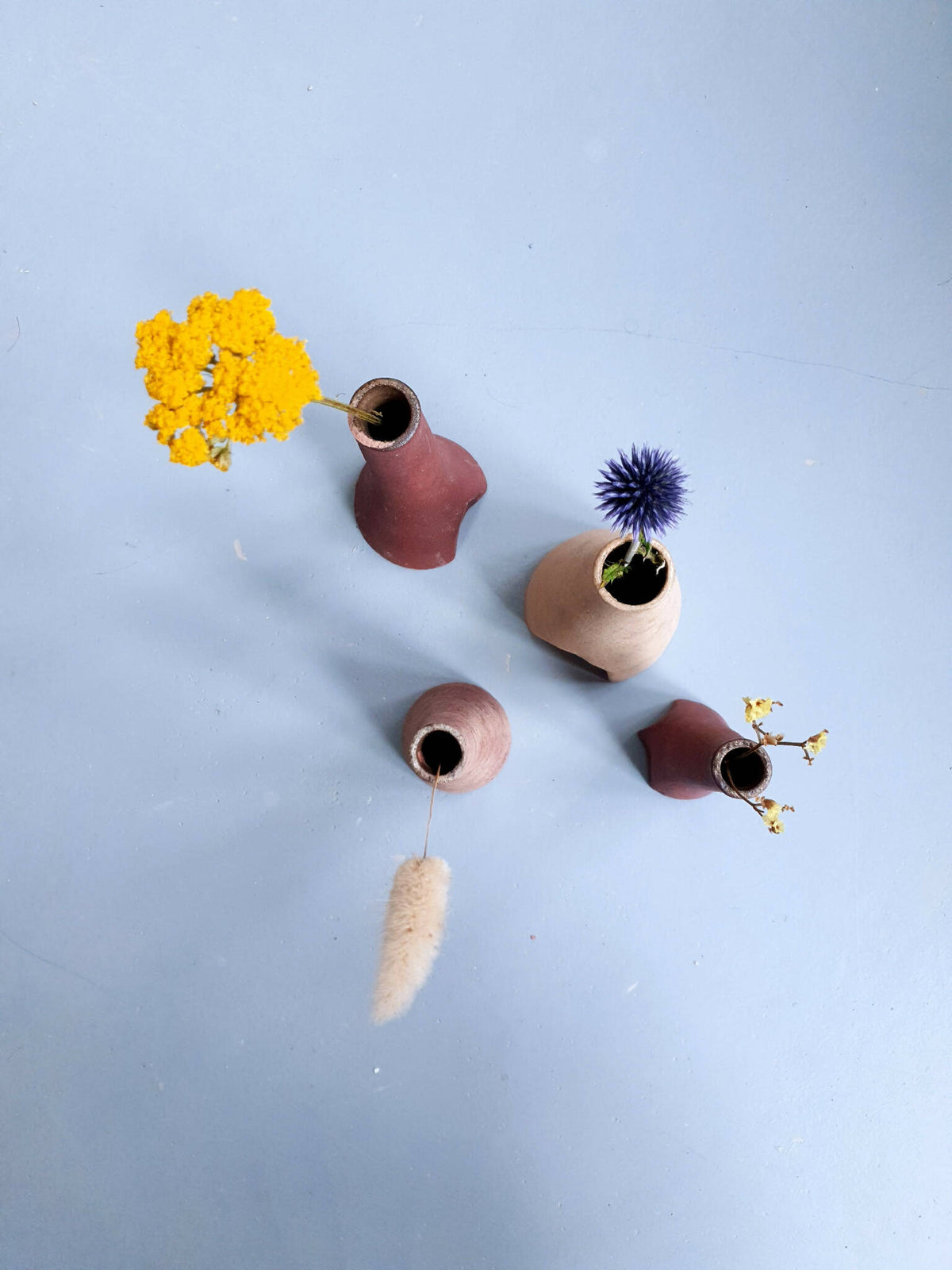 Quatre petits vases décoratifs épars bordeaux, rose et beige, ouverts et fleuris