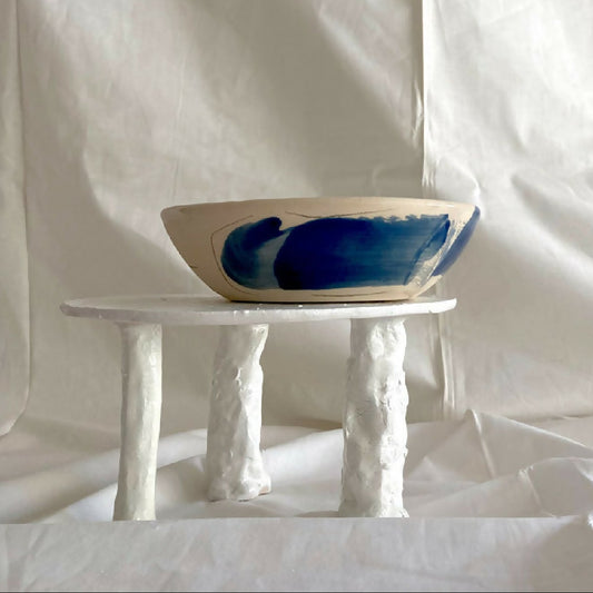 Bol en grès blanc avec motif bleu abstrait, sur pieds de présentation.