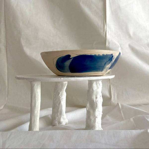 Bol en grès blanc avec motif bleu abstrait, sur pieds de présentation.