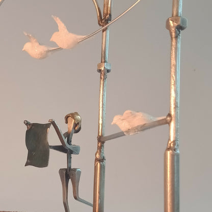 Figurine en robe noire tenant une canne, sur manège décoratif, avec oiseau en blanc.