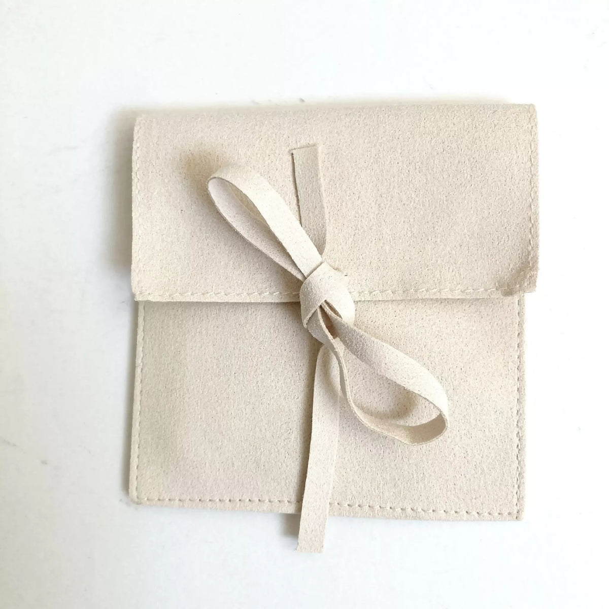 Bracelet en cordon blanc avec perle dorée sur pochette beige