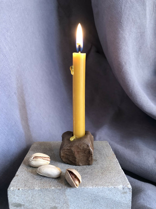 Mini bougeoir en pierre sombre avec bougie jaune allumée, base carrée et coquillages
