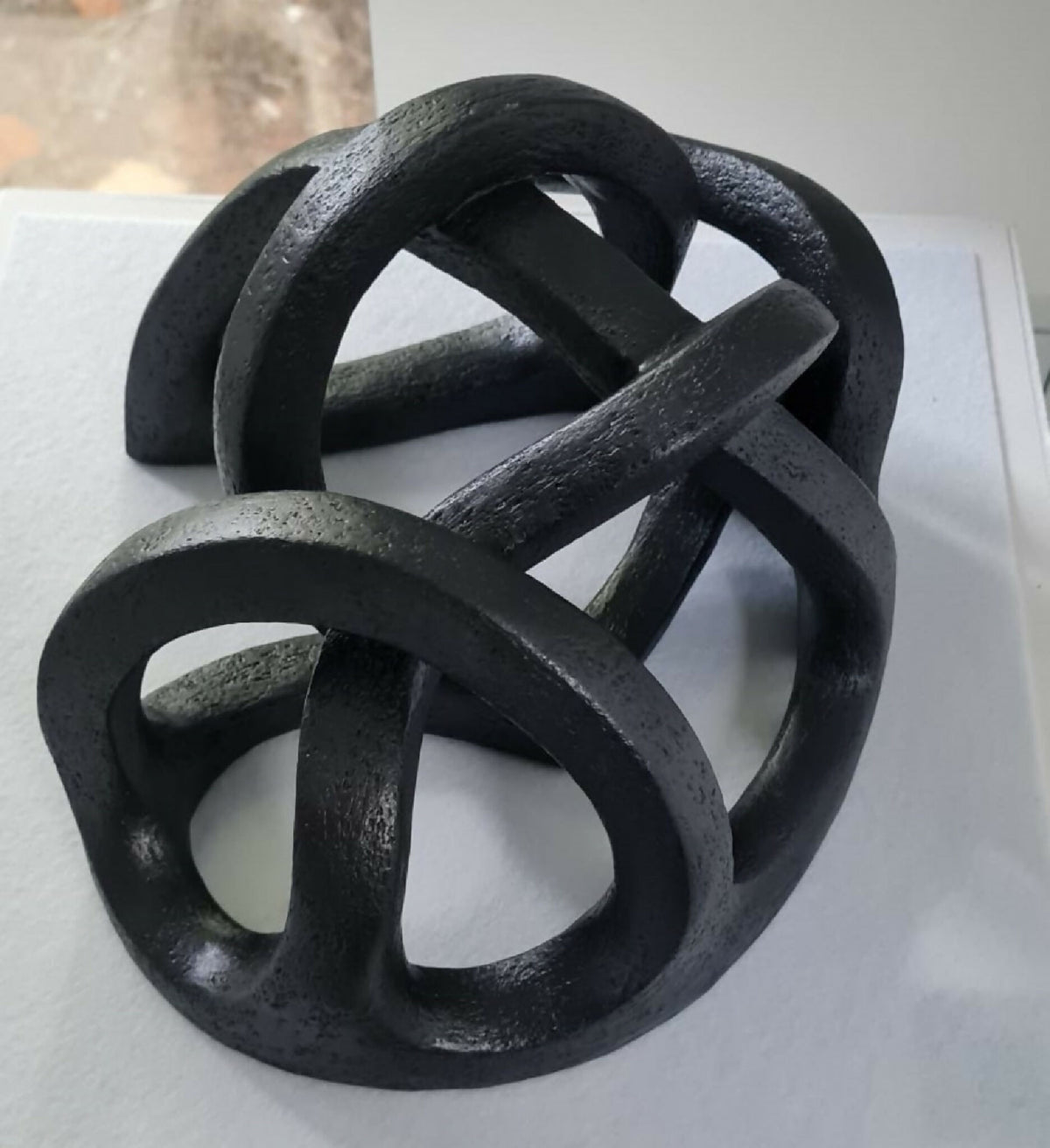 Sculpture abstraite en argile sombre sur socle, anneaux entrelacés.