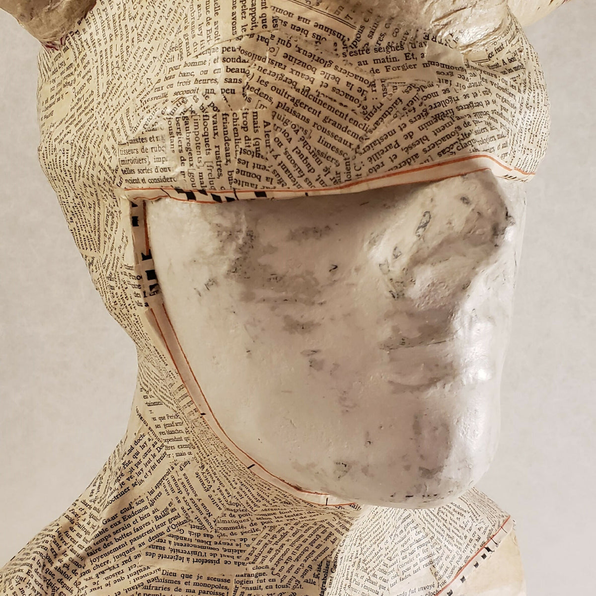 Buste sculpté: gros plan du visage masqué en papier texturé beige, détails et bords visibles