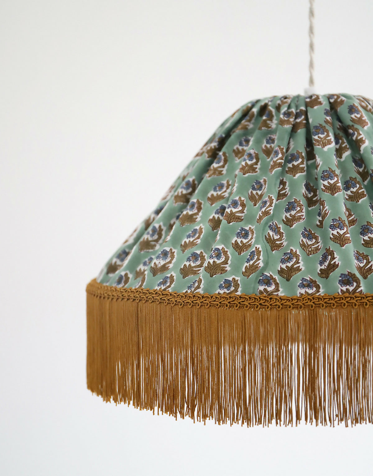 Suspension vue rapprochée : abat-jour vert à motifs floraux, franges dorées au bord.