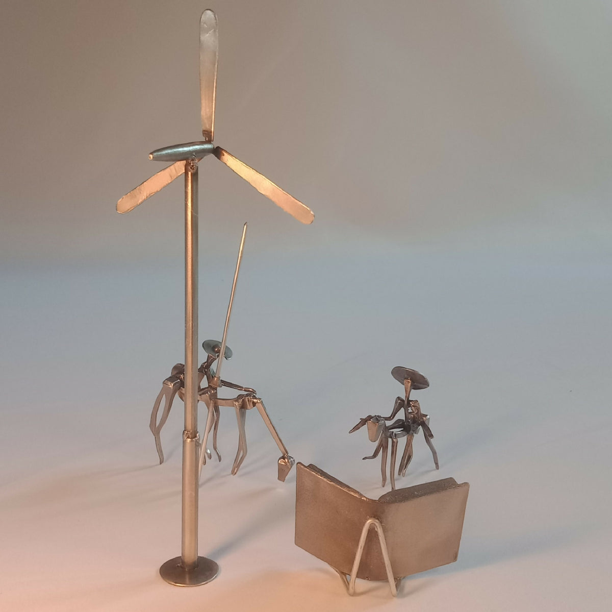 Sculpture en acier : chevalier sur mât, cape et personnages autour du livre.