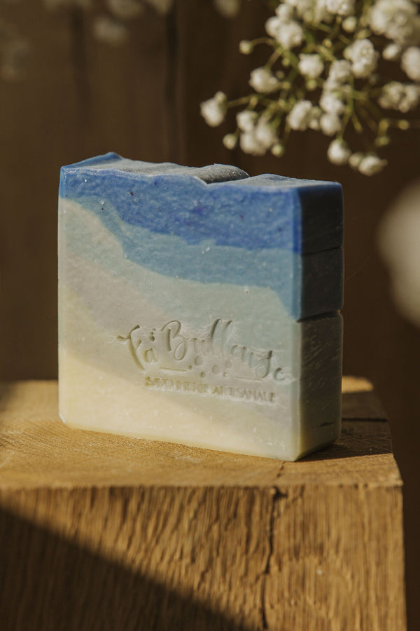 Savon rectangulaire bleu et beige, face avant avec logo gravé, près de fleurs