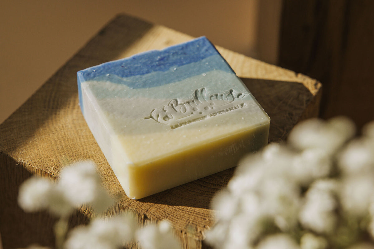 Savon artisanal rectangulaire bleu et beige, posé sur toile de jute, vue en angle