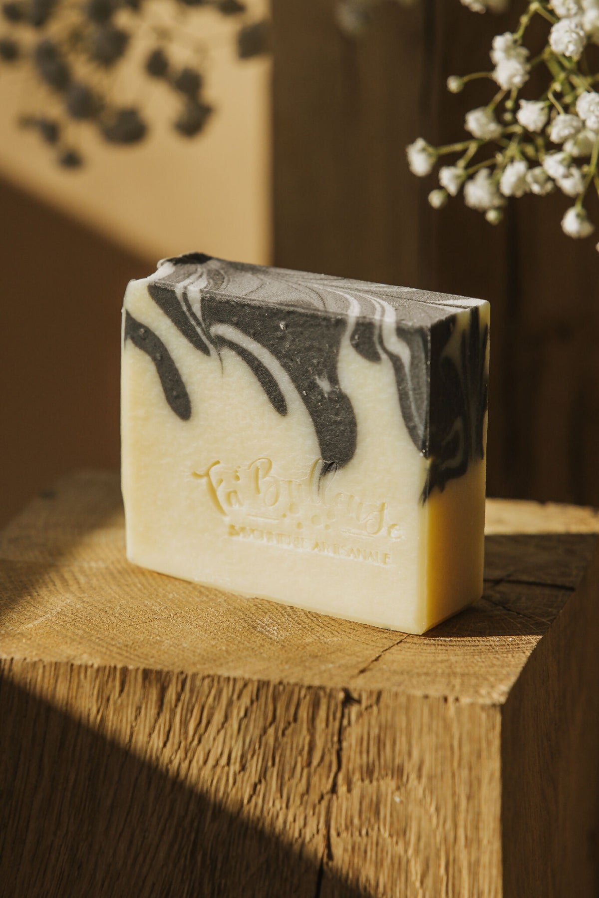 Savon solide au charbon actif, barre crème à marbrures noires, face marquée.