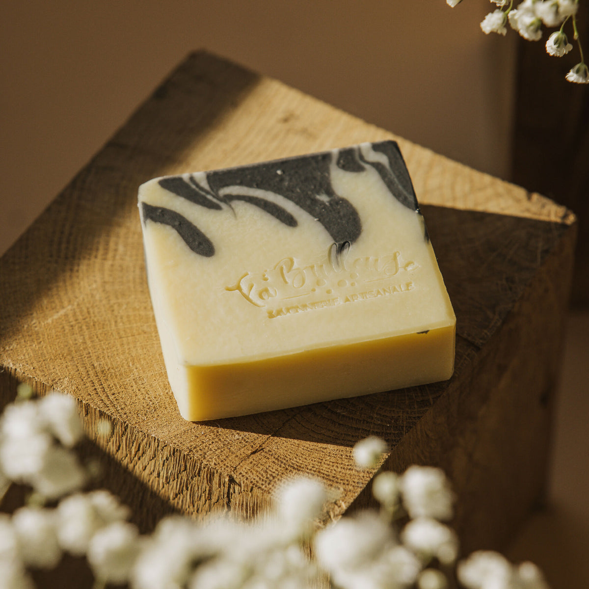 Savon solide au charbon actif et karité, barre crème marbrée sur support en bois.