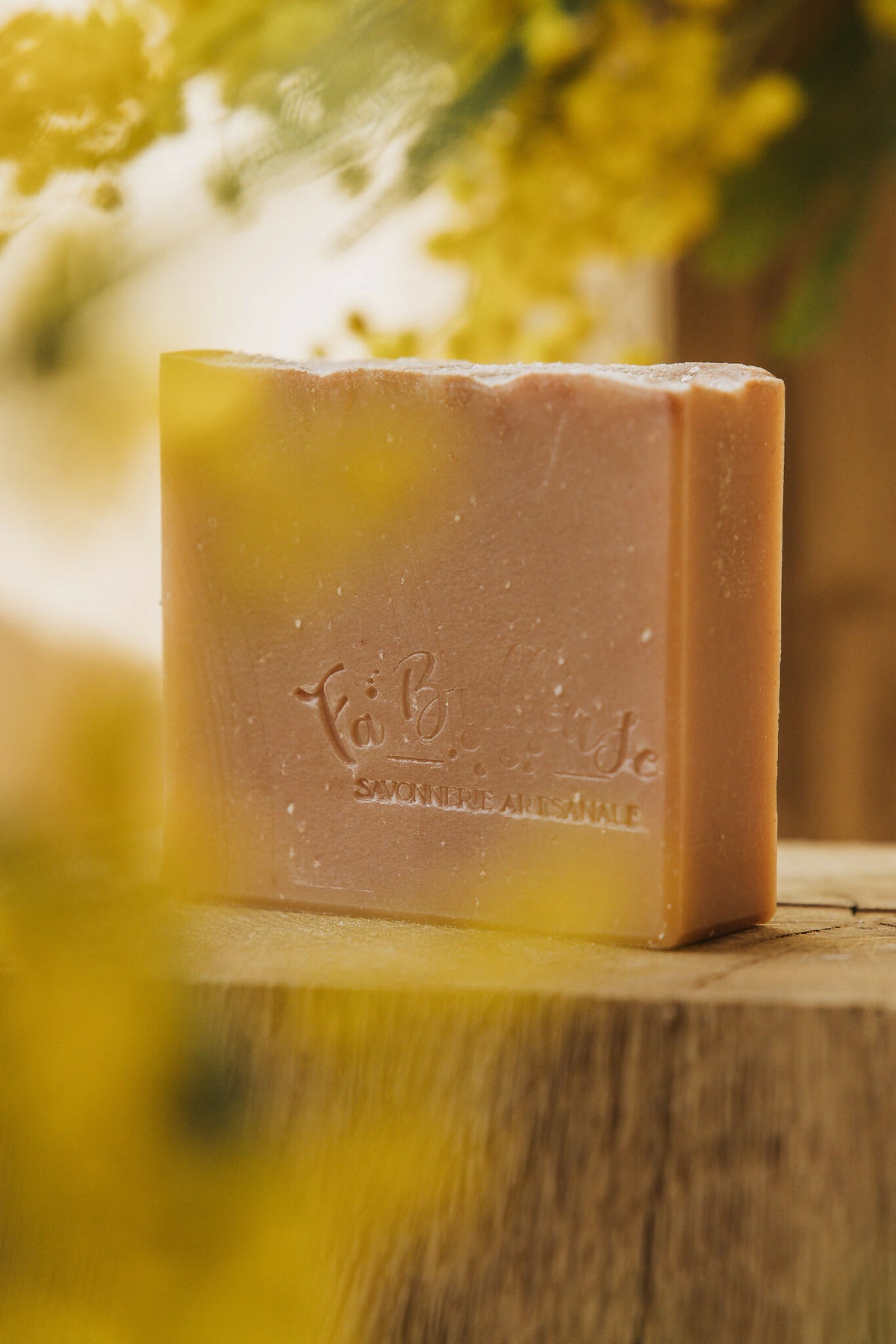 Savon artisanal en barre, teinte ambrée, logo gravé et surface texturée.