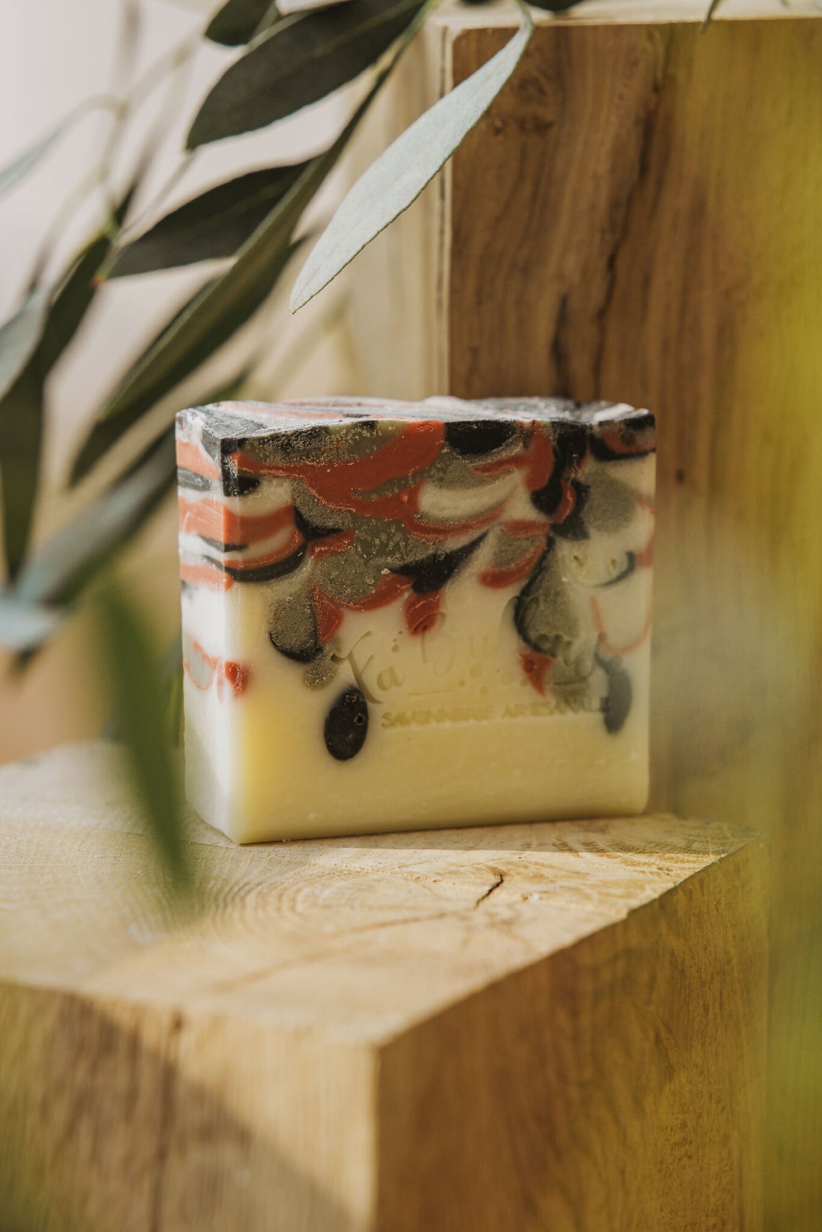 Savon solide rectangulaire jaune pâle, dessus marbré noir et motifs rouges.