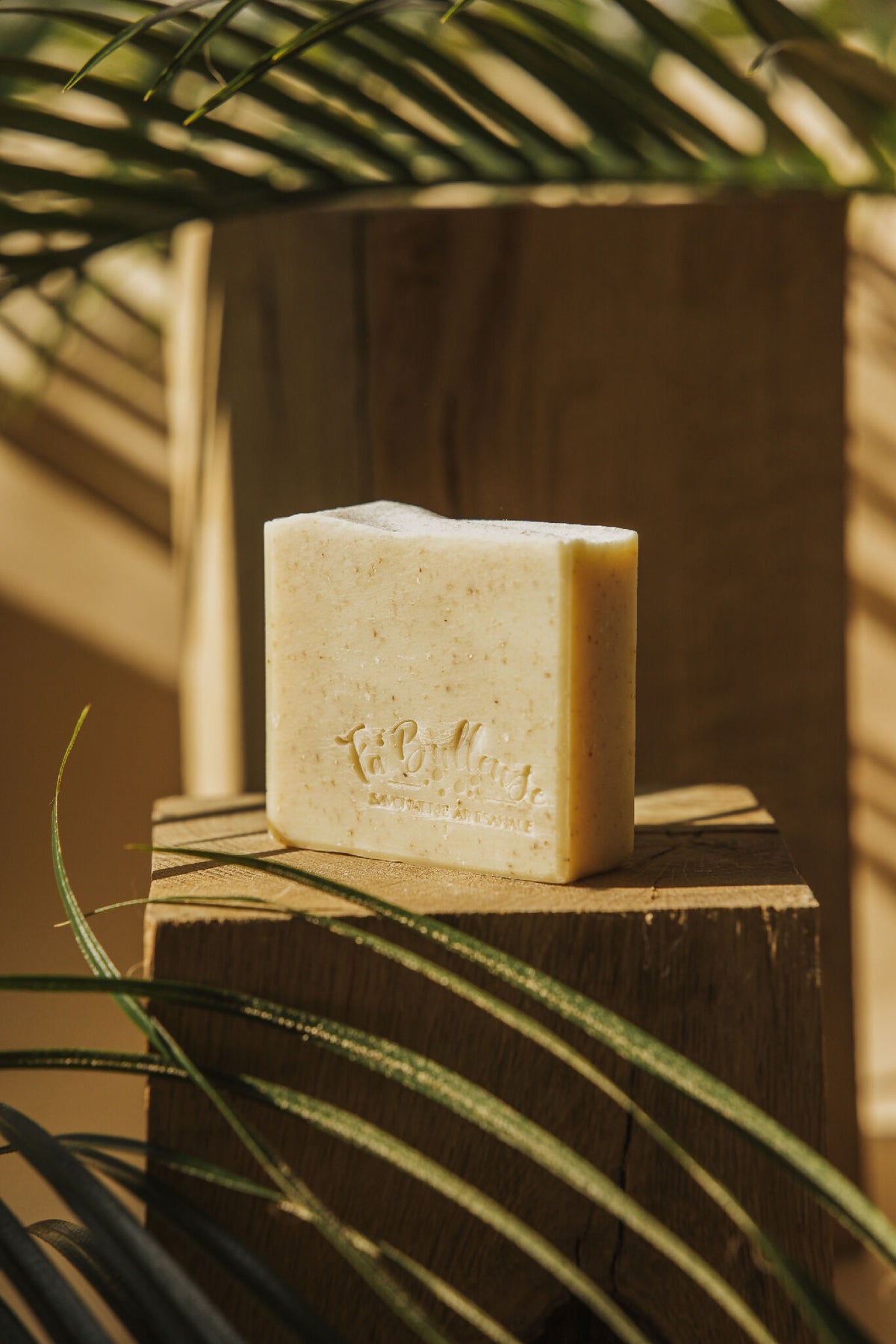 Savon en barre crème avec logo gravé, posé sur une planche de bois.