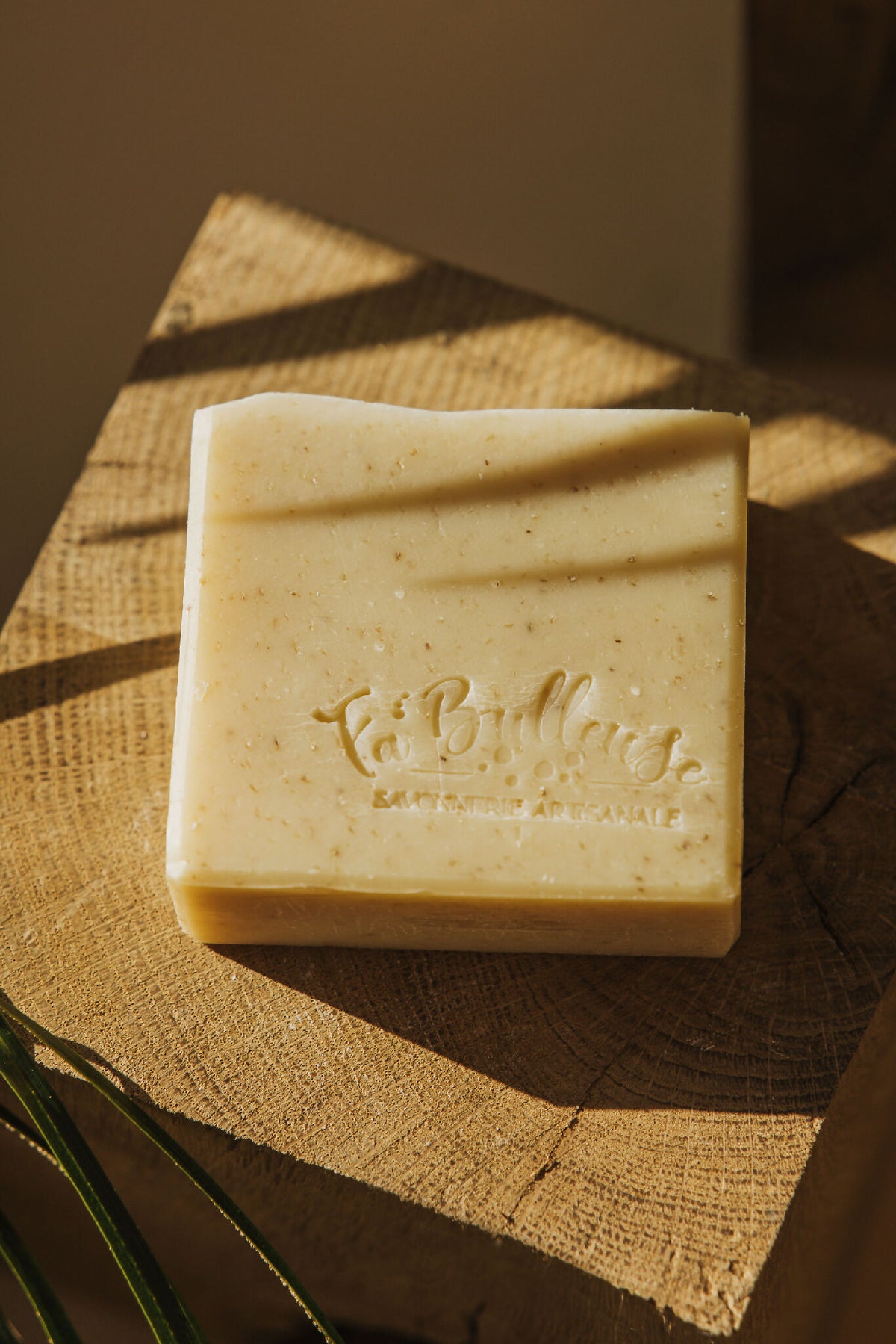 Savon rectangulaire crème, logo en relief, posé sur une tranche de bois.