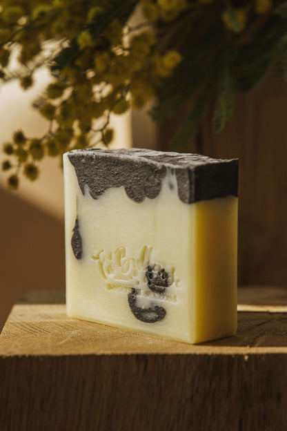 Savon au patchouli et charbon végétal, cube blanc avec dessus gris foncé.