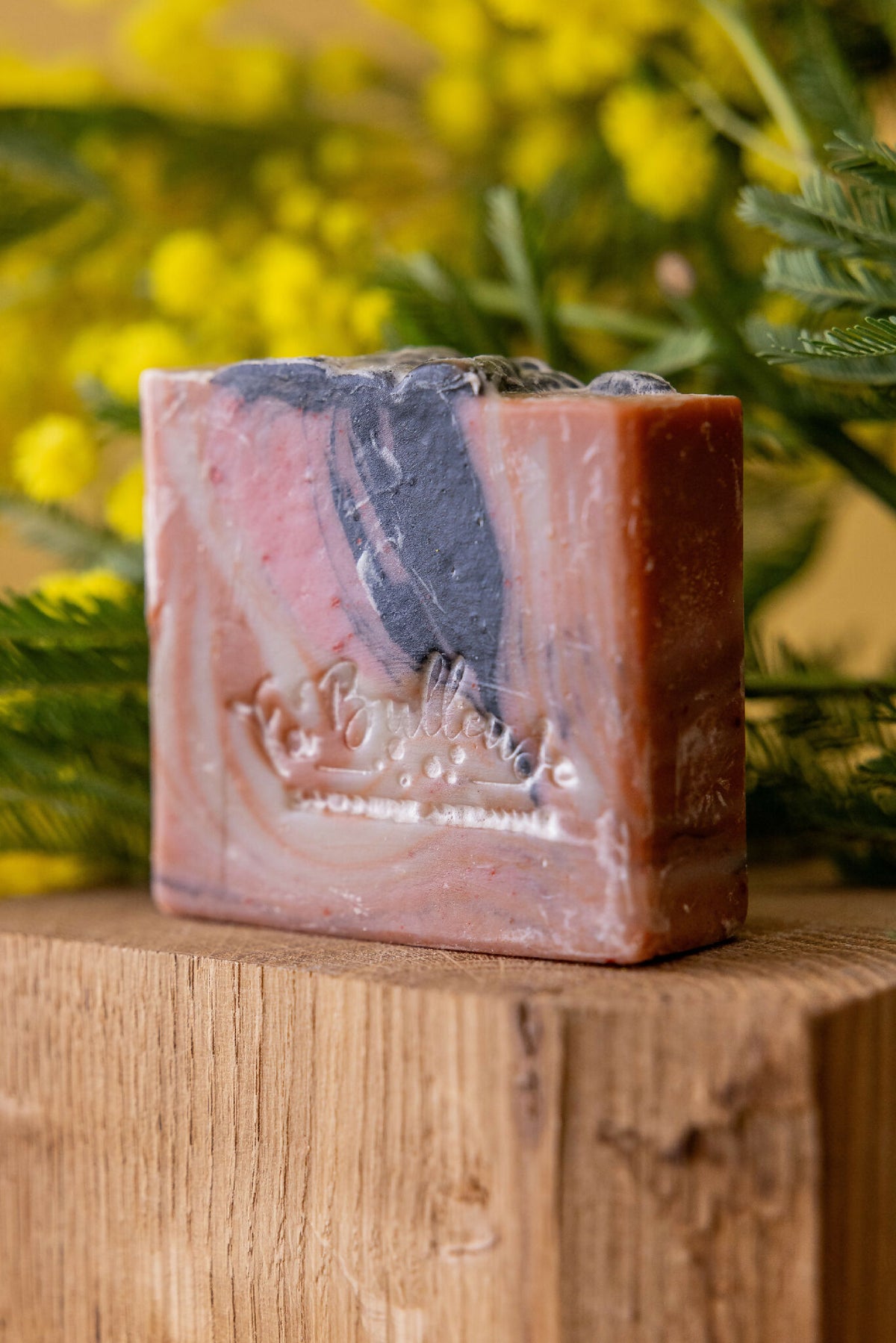 Savon artisanal en barre marbrée rosé, beige et noir sur plateau en bois.
