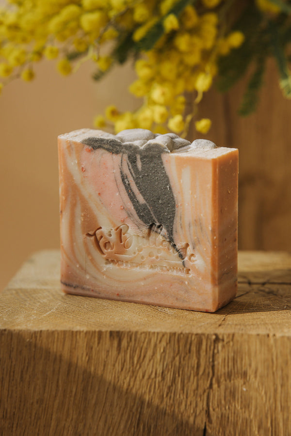 Savon en barre marbrée beige, rosé et noir, posé sur une planche en bois.
