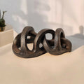 Sculpture abstraite en argile sombre sur socle, arches et anneaux entrelacés.