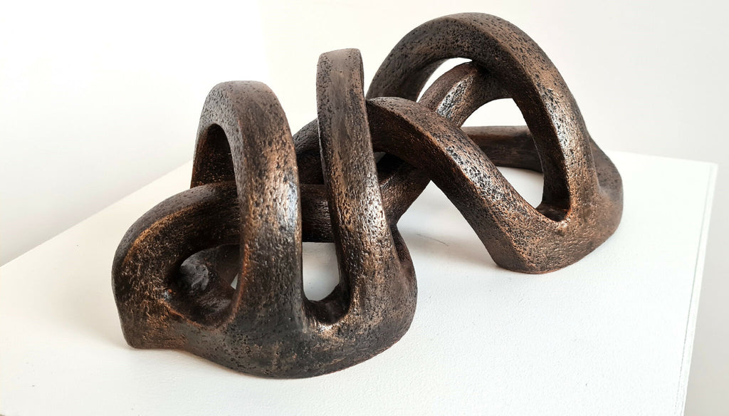 Sculpture en argile sombre abstraite, plusieurs anneaux courbés et évidements.