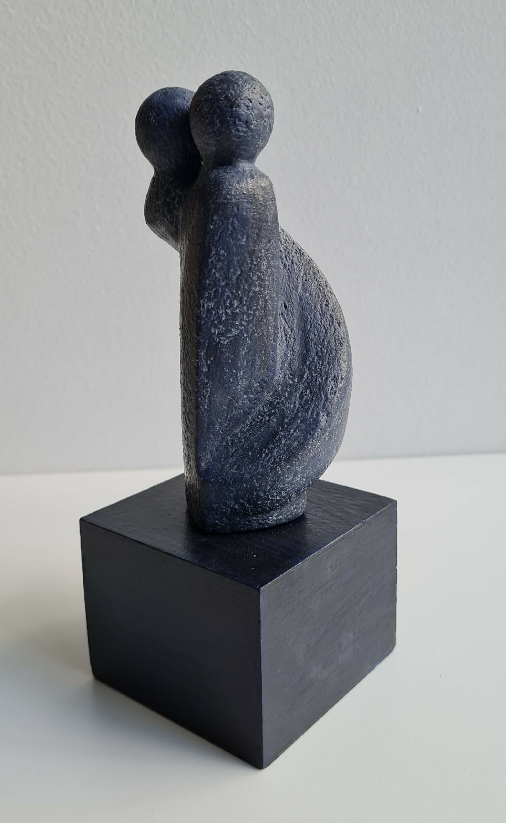 Sculpture couple bleu foncé, dos visible, sur socle cubique noir