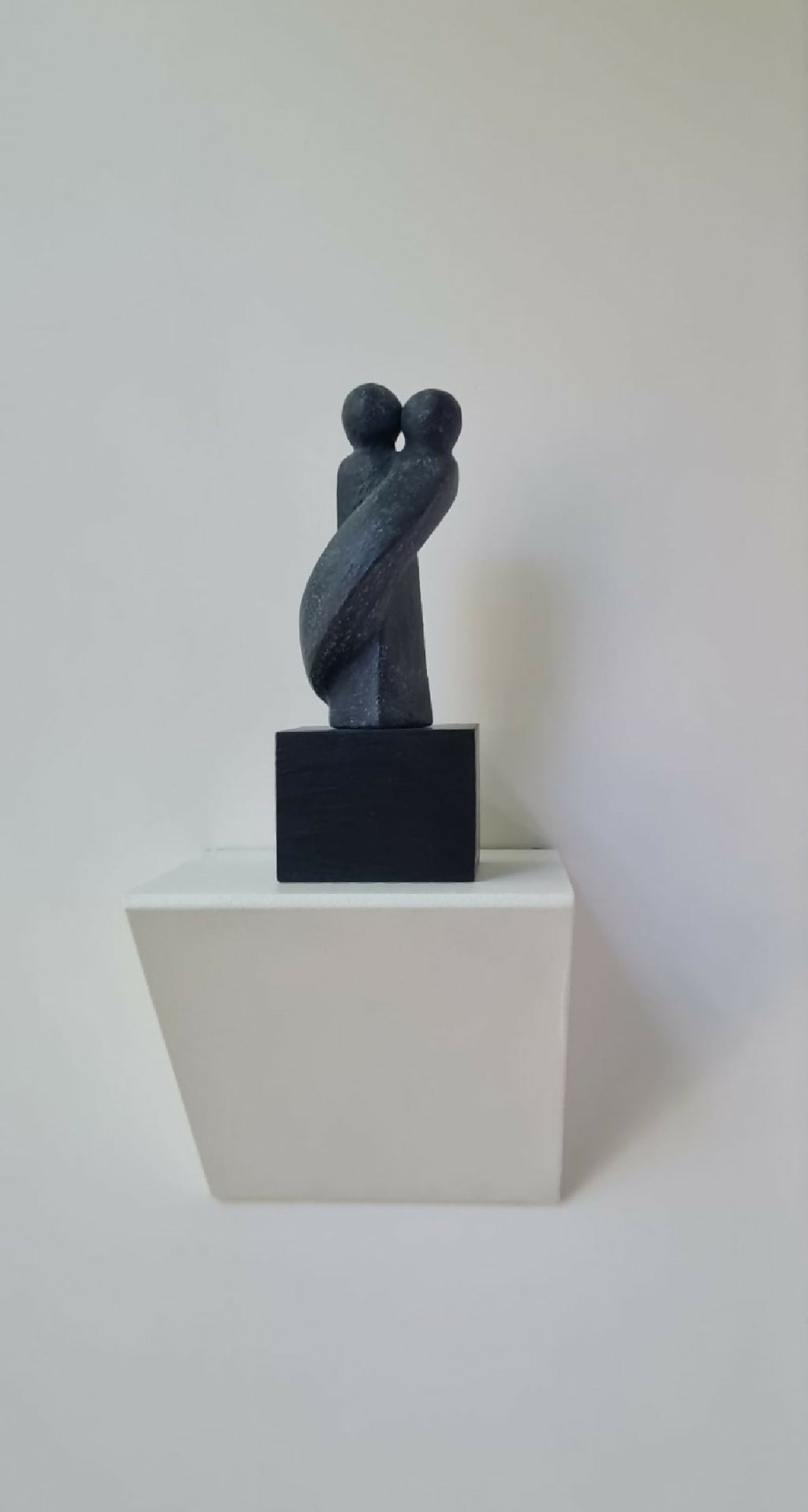 Sculpture couple bleu nuit posée sur un socle noir, sur support blanc
