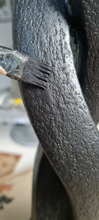 Détail d’une sculpture en argile sombre : texture granuleuse et main