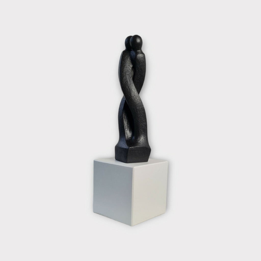 Sculpture en argile sombre de deux corps enlacés, sur socle blanc