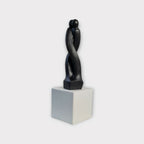Sculpture en argile sombre de deux corps enlacés, sur socle blanc