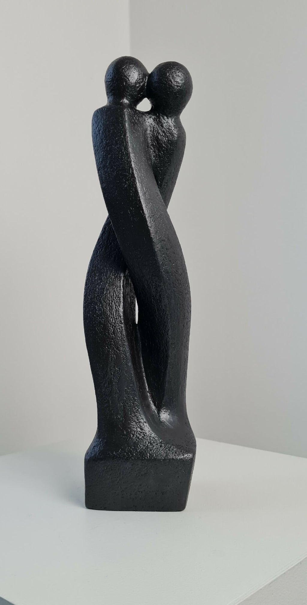 Sculpture en argile sombre : deux personnages enlacés de profil sur socle