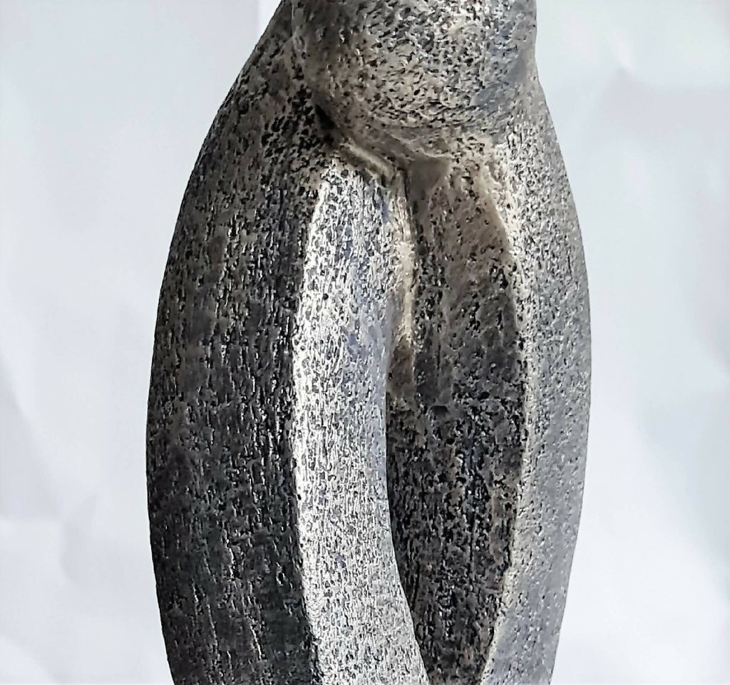 Sculpture en argile grise texturée, deux formes entrelacées avec ouverture en U.