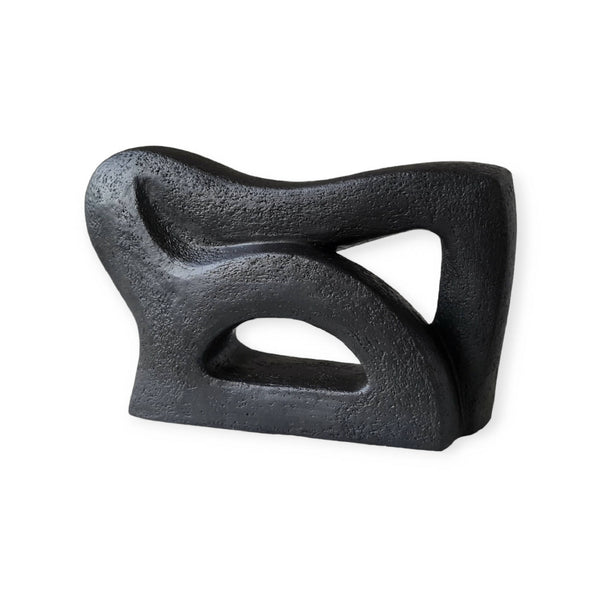 Sculpture abstraite en pierre sombre avec ouvertures en forme d’arcs, finition texturée.