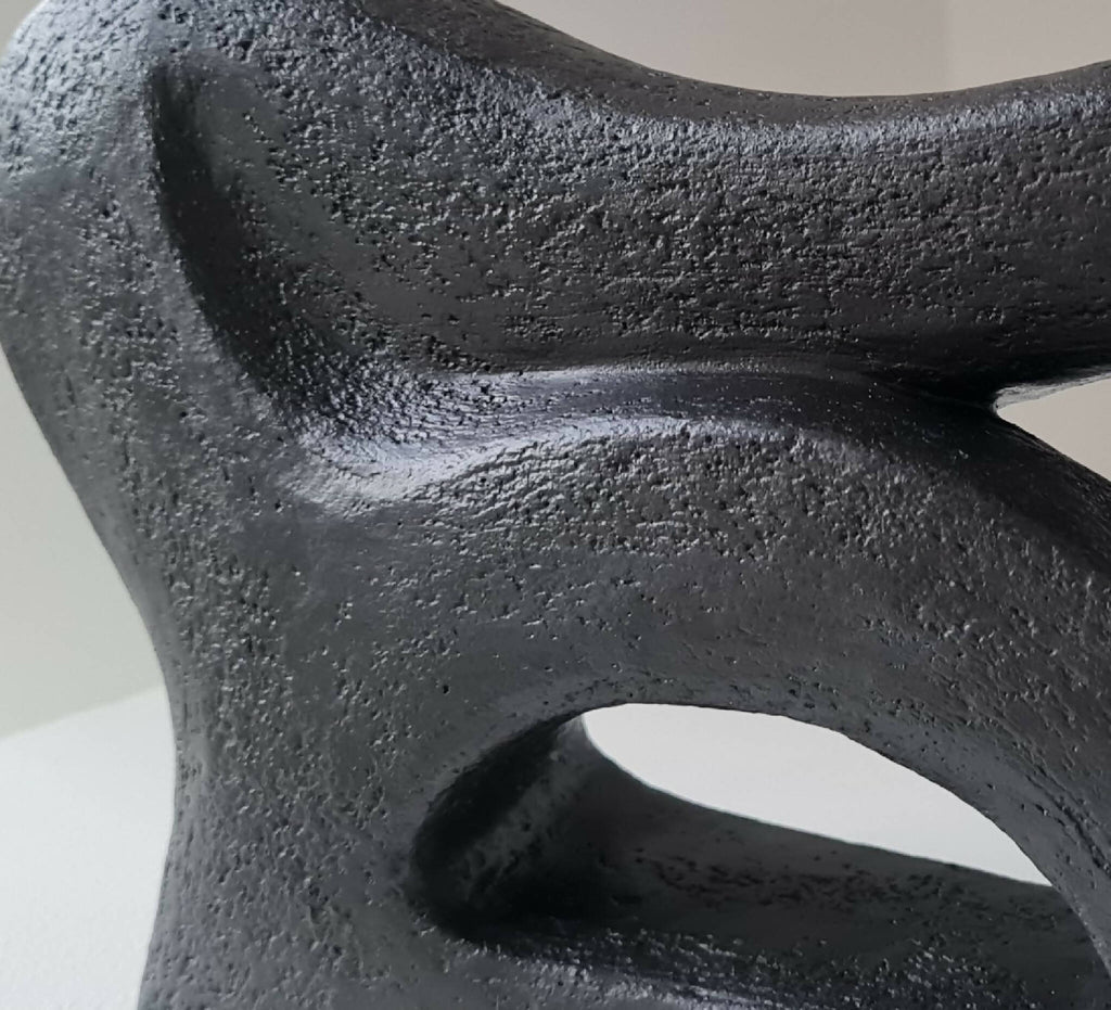 Détail de sculpture abstraite sombre, surface rugueuse et ouvertures découpées.