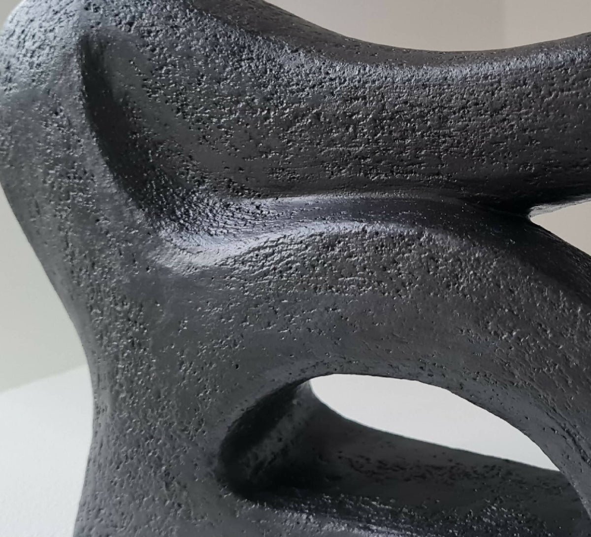 Détail de sculpture abstraite sombre, surface rugueuse et ouvertures découpées.