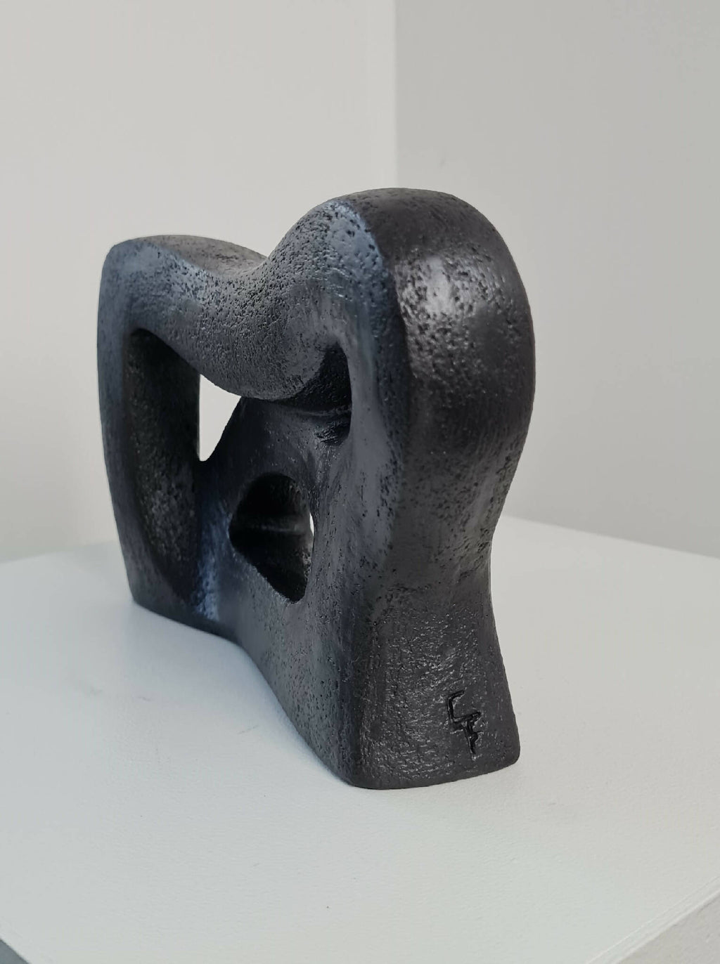 Sculpture abstraite sombre sur socle, formes courbes avec grands vides découpés.