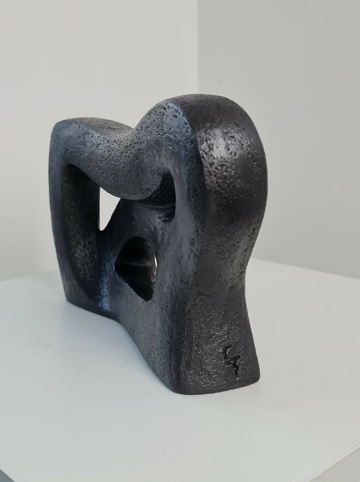 Sculpture abstraite sombre sur socle, formes courbes avec grands vides découpés.