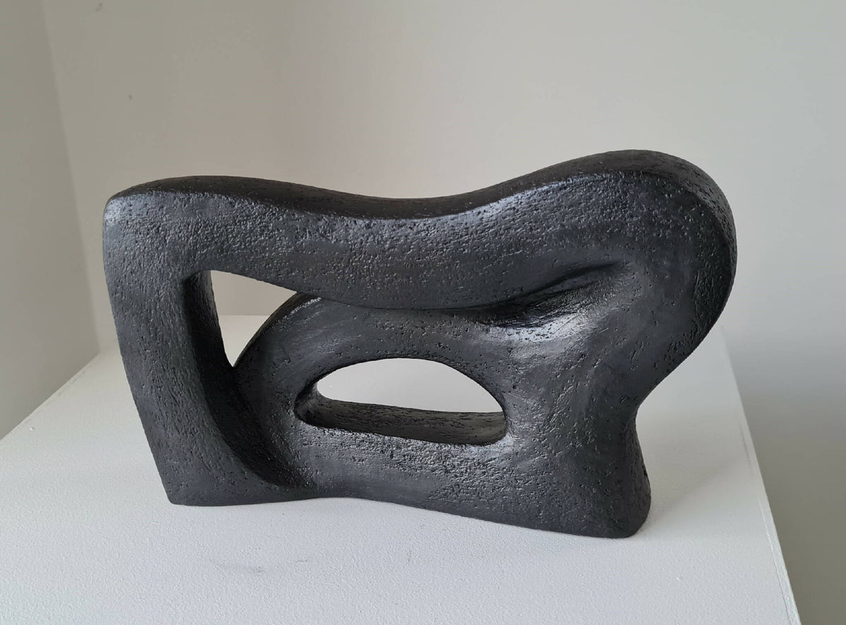 Sculpture abstraite sombre aux courbes sinueuses, trois ouvertures ovales visibles.
